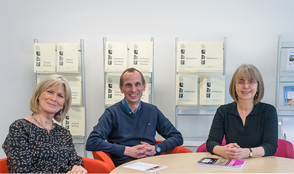 Three well dressed adults round a table smiling at the camera