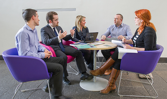 A committee meeting of 5 people taking place round a small table