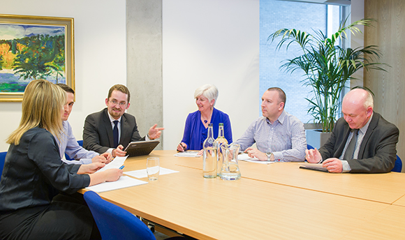 A committee meeting taking place at a board room table 