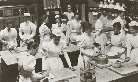 B+W photo of a kitchen full of women in Edwardian style chef's whites