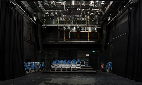 Empty performance room with folding chairs set up on the risers and a large light rig