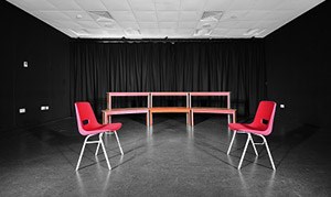 A dimly lit performance studio with two empty chairs centre stage, QMU