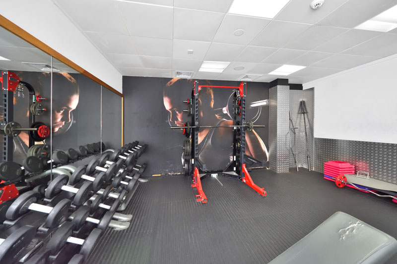 A bright, modern weights room in the gym with a large variation in weights & a squat rack