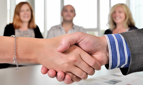 Close up of a pair of shaking hands, 3 people smile on in the background