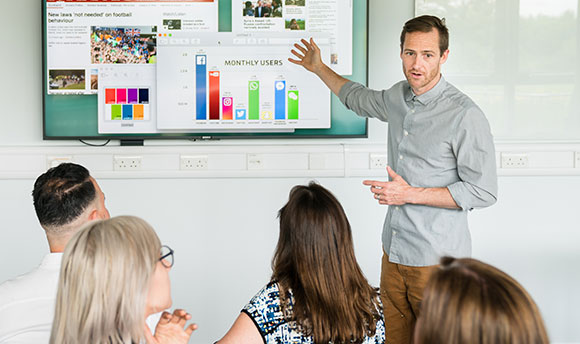 A lecturer giving a presentation on user statistics to a digital communications class 