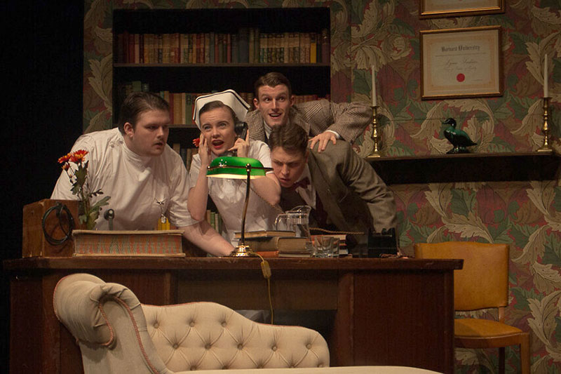 QMU drama students hunched over a desk listening into a "call" in retro costumes