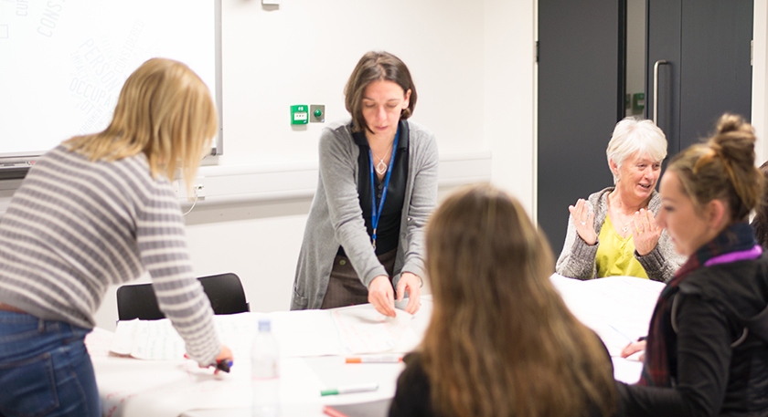 A group of Queen Margaret University Students and lecturer chatting around a table