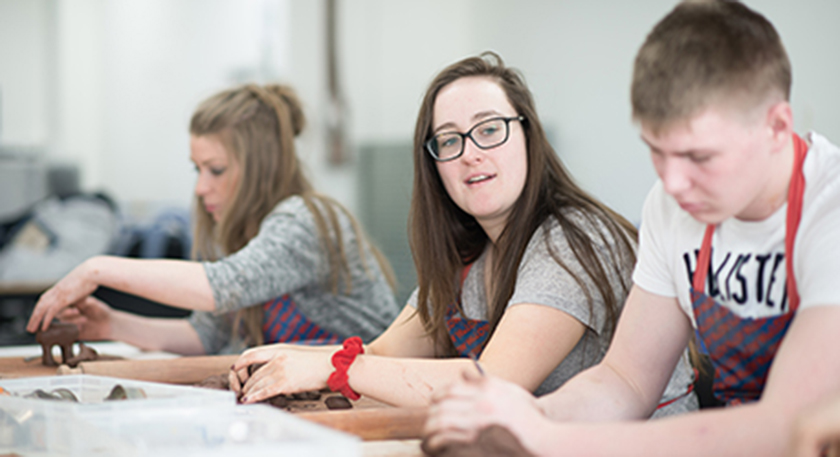 A row of students with aprons on making things out of modelling clay