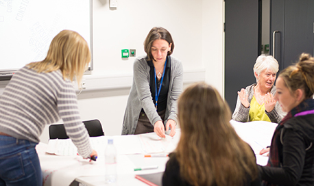 A group of Queen Margaret University Students and lecturer chatting around a table