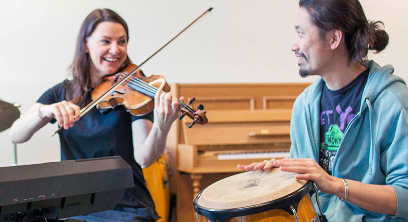 A smiling violinist and a drummer playing a bongo