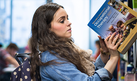 A student pulling an occupational therapy book out of a library bookshelf