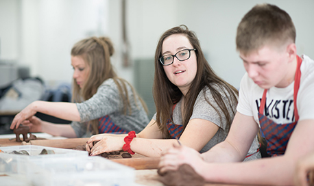 A row of students with aprons on making things out of modelling clay