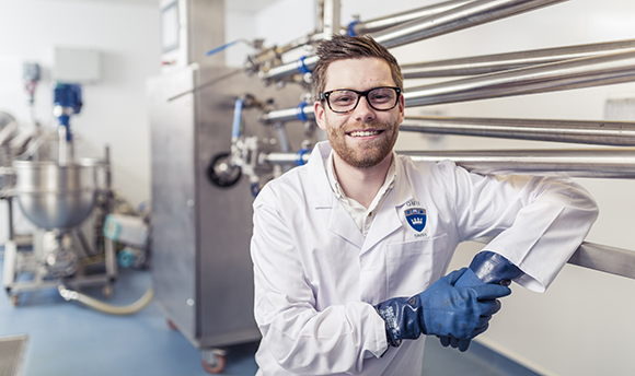 QMU student smiling at the camera in a lab coat and protective gloves