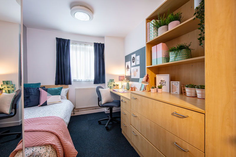 Inside a standard room, including a single bed, desk, mirror and chair 