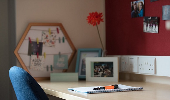 A student accommodation desk with some photographs and a notebook on it