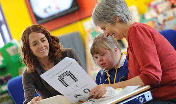 A young girl with Downs Syndrome using the speech and language therapy equipment with two adults