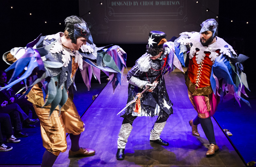 Three performers in the 2024 QMU Costume Showcase, one is dressed as a fairytale-style nutcracker while the other two are styled as birds.