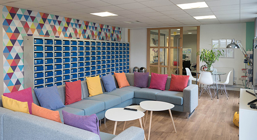 A large common area with a very large sofa, tables and lockers along the wall