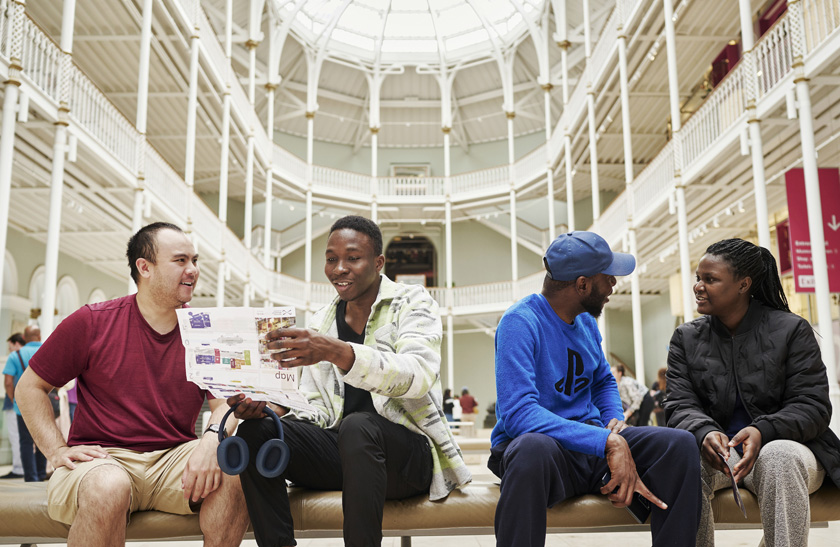 A group of four young people taking a seat on a bench inside the National Museum of Scotland