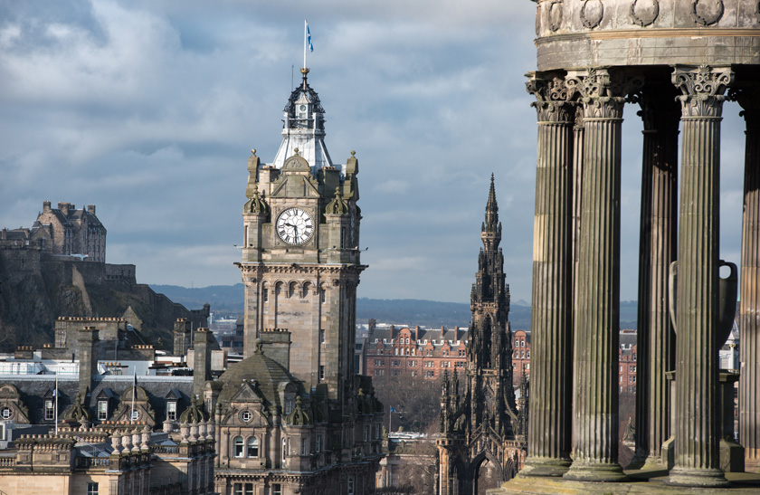 A view of Edinburgh's cityscape, including Edinburgh Castle, the Balmoral Hotel clock tower, the Scott Monument, and the Dugald Stewart monument on Calton Hill