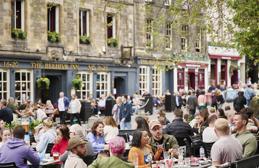 A crowd of people enjoying food and drinks in the sunshine in Edinburgh's Grassmarket